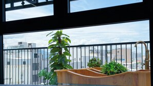 Un dormitorio con cama y lavamanos de madera, y vista de la ciudad desde un balcón con baranda negra.
