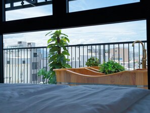 A bedroom with a wooden bed, a wooden sink, and a view of the city through a balcony with a black railing. - La Van Residence (Da Nang)
