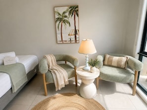 Een hotelkamer met een bed, twee fauteuils, een lamp, een schilderij en een welkomstbord.