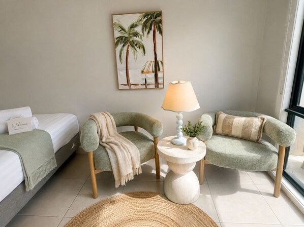 Una habitación de hotel con una cama, dos sillones, una lámpara, un cuadro y un cartel de bienvenida.