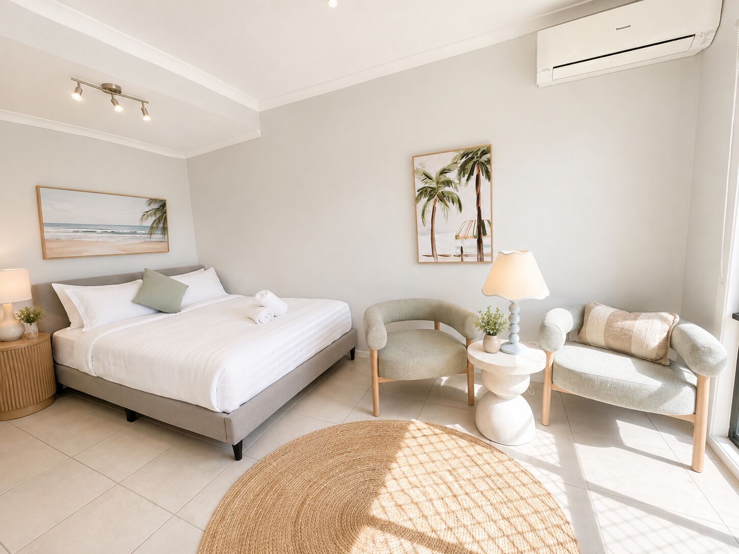 A modern bedroom with a bed, two chairs, a round rug, and wall art.