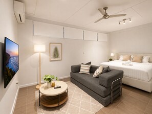 Una habitación de hotel moderna con cama, sofá, una mesa redonda de centro, televisor y ventilador de techo.
