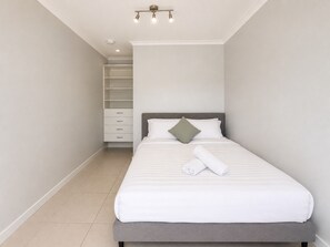 Een slaapkamer met een bed, nachtkastje, kast en een lamp.