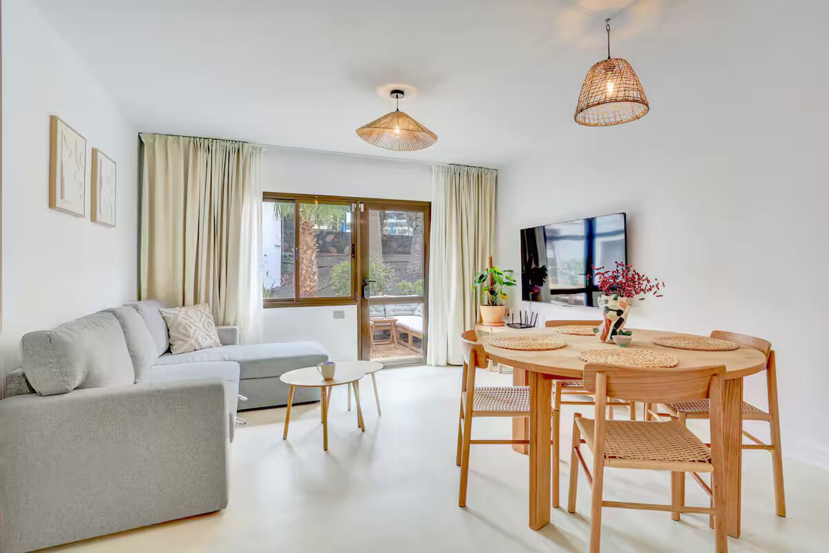 A modern living room with a sofa, dining table, chairs, and a TV.