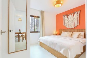 A bedroom with a bed, a bedside table, a hanging macrame wall decoration, and a window with curtains. - Brand New Apt - Oasis Duna pools (Corralejo)