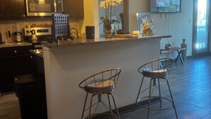 A modern kitchen with a central island, bar stools, a microwave, and a TV mounted on the wall. - City Views. Luxury Vibes. West Midtown Living. (Atlanta)