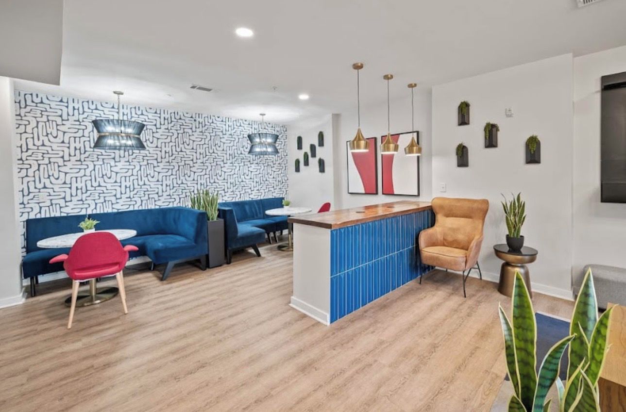 A modern lounge area with a blue sofa, a red chair, a wooden reception desk, and a patterned wall.