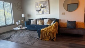 A living room with a blue sofa, a round mirror, and a painting on the wall. - City Views. Luxury Vibes. West Midtown Living. (Atlanta)
