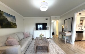 A living room with a sofa, coffee table, TV, and a painting on the wall. - Cozy 2-bedroom, beautifully decorated, great location. (Oxford)