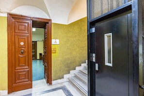 A hotel entrance with a wooden door and a black elevator door. - Napoli Chantant (Naples)