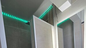 A bathroom with a white sink, a mirror, and green LED lights along the ceiling. - Cozy beachfront studio (Brem-sur-Mer)