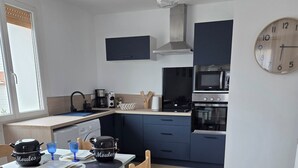 A modern kitchen with a dining table, chairs, and a clock on the wall. - Cozy beachfront studio (Brem-sur-Mer)