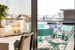 A view from a room with a large window overlooking a marina with multiple sailboats. Inside, there is a table with chairs and a small potted plant.
