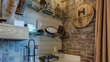 A kitchen with a brick wall, wooden shelves, a clock, and a whiskey barrel sign.
