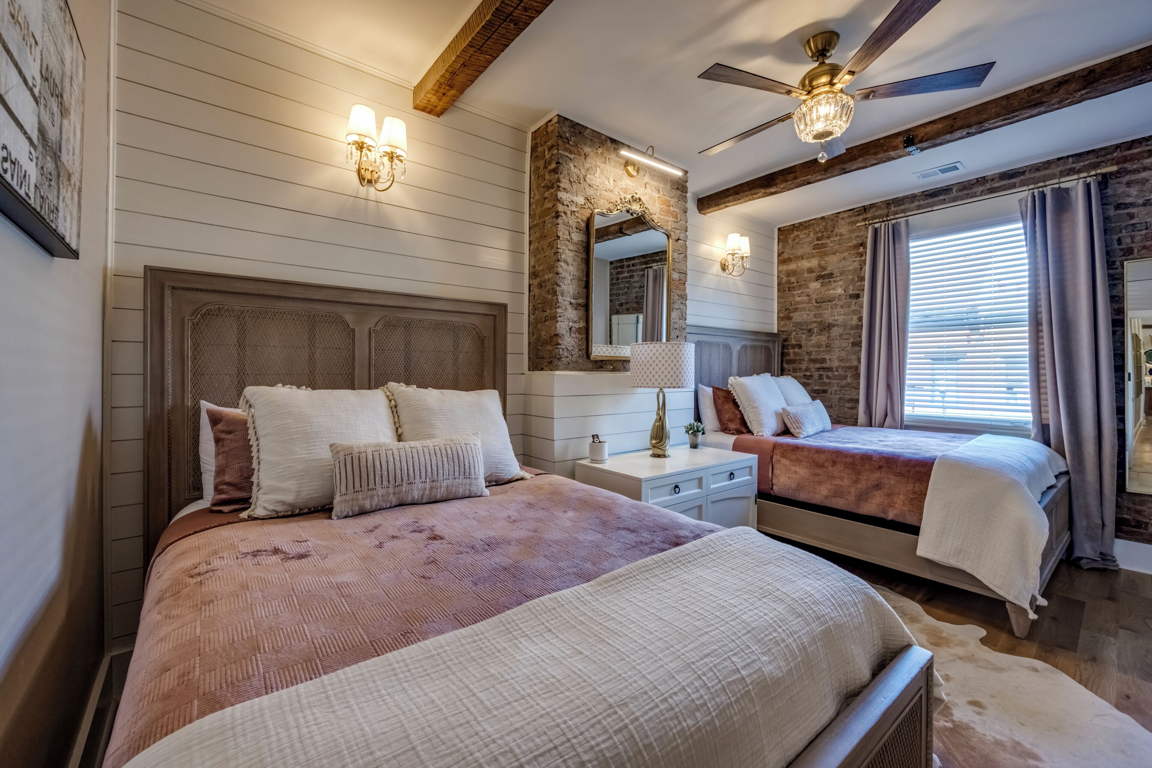 A bedroom with two beds, a ceiling fan, and a large mirror.