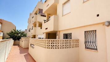 Un edificio residencial de varios pisos con balcones, un patio con baldosas y una valla decorativa.