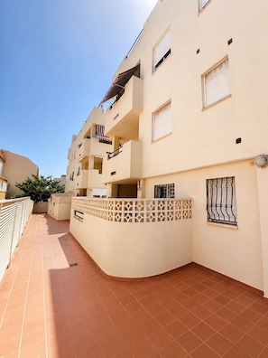 Un edificio residencial de varios pisos con balcones, un patio con baldosas y una valla decorativa.