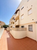 Un edificio residencial de varios pisos con balcones, un patio con baldosas y una valla decorativa.