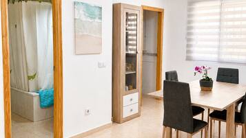 Una habitación con mesa de comedor, sillas, zona de ducha y un armario con cajones.