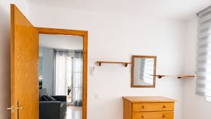 Un dormitorio con un aparador de madera, una cama, un espejo y una puerta que da a una sala de estar.
