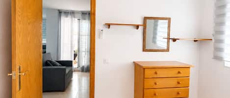 Quarto com penteadeira de madeira, uma cama, espelho e porta para uma sala de estar.
