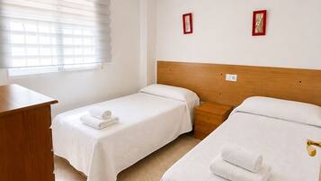 Habitació d'hotel amb dos llits individuals, un panell de fusta al capçal, una taula de nit, un escriptori i un ventilador de sostre.