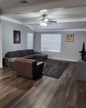 A living room with a sectional sofa, a coffee table, a rug, a ceiling fan, and a TV. - High Ceilings 2-bedroom house in enjoyable Elgin with Backyard (Elgin)