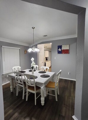 A dining area with a table set for four, white chairs, a chandelier, and a Texas flag decoration. - High Ceilings 2-bedroom house in enjoyable Elgin with Backyard (Elgin)