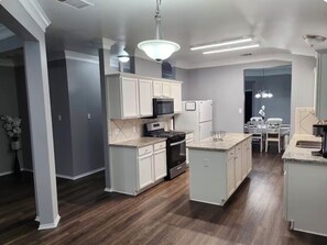 A modern kitchen with white cabinetry, a central island, and a dining area with a table and chairs. - High Ceilings 2-bedroom house in enjoyable Elgin with Backyard (Elgin)
