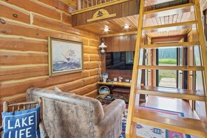 A log cabin interior with a wooden chair, a painting, a television, and a ladder. - Tranquil 1-bedroom cabin - The Stuga- on Lake Superior's South Shore! (Port Wing)