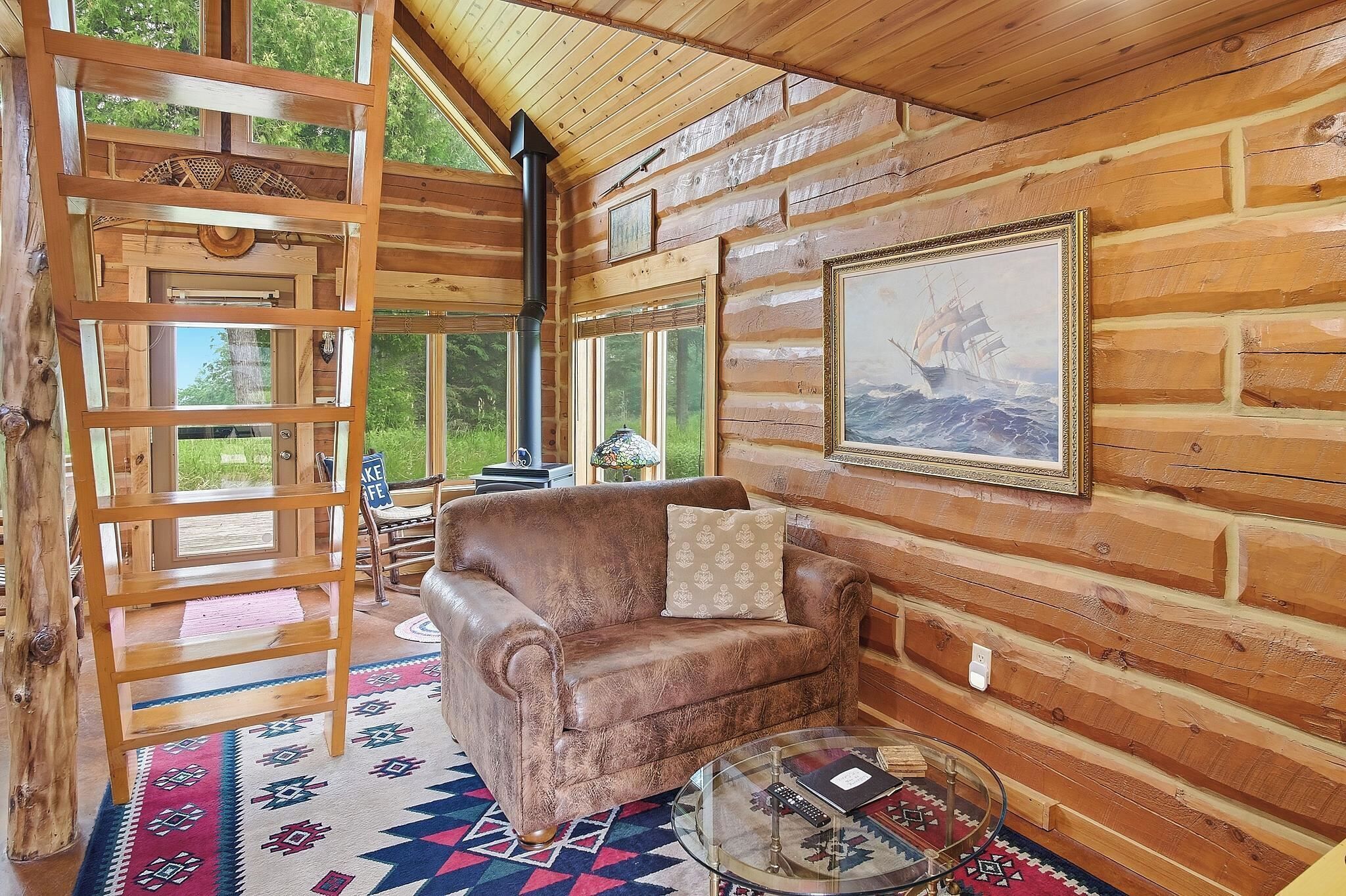 A cozy cabin interior with a leather sofa, a patterned rug, and a large window offering a view of the outdoors.