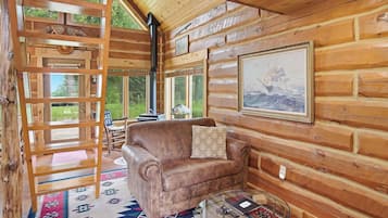 A cozy cabin interior with a leather sofa, a patterned rug, and a large window offering a view of the outdoors.