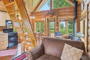 A cabin interior with a wooden staircase, a sofa, a table, and a stove.