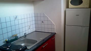 A kitchen with a sink, red cabinets, a white refrigerator, and a microwave.