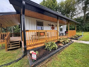 Une terrasse en bois avec un porche couvert, un coin repas avec du mobilier d’extérieur et un jardin avec des plates-bandes surélevées.