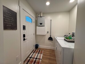 A laundry room with a washing machine, a broom, and a sign on the door.