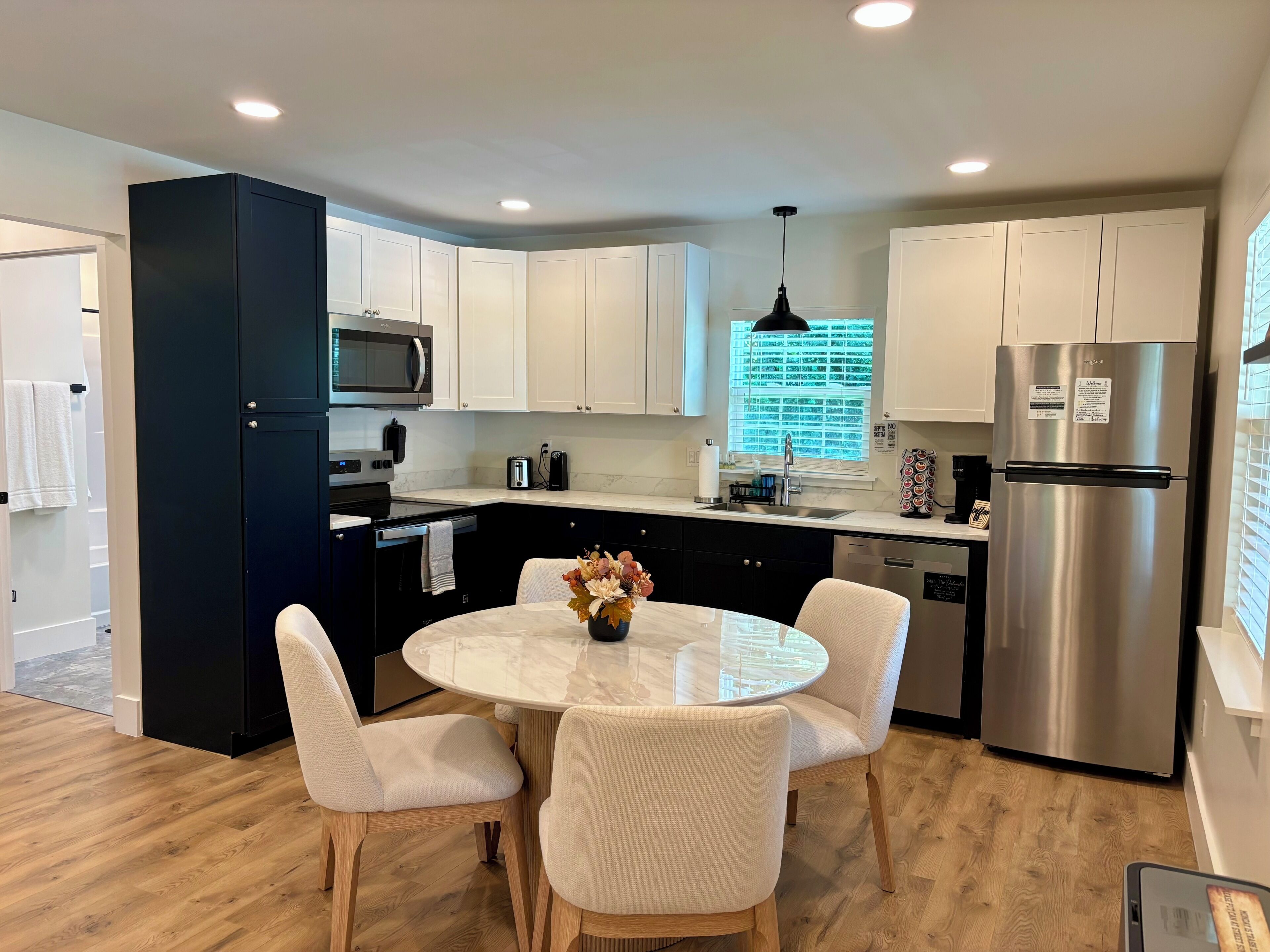 A modern kitchen with white cabinets, stainless steel appliances, and a round dining table with chairs.