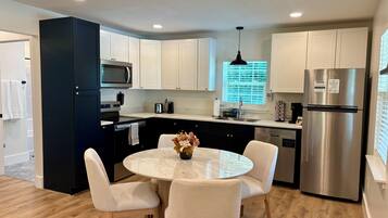 A modern kitchen with white cabinets, stainless steel appliances, and a round dining table with chairs.