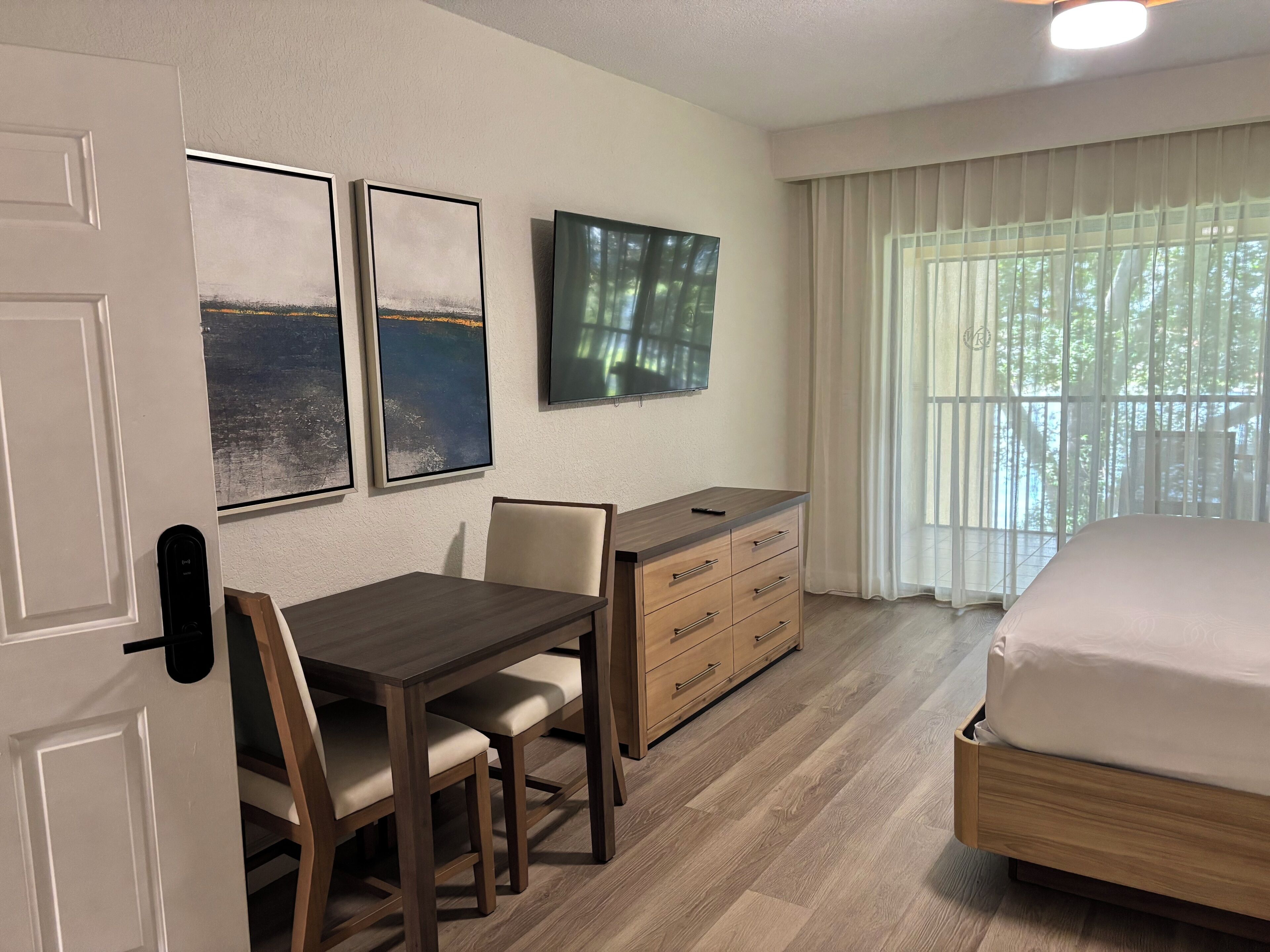 Habitación de hotel con cama, escritorio con silla, cómoda y obras de arte en la pared.