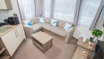 A modern living room with a beige sofa, a wooden coffee table, and a kitchen area with a stove.