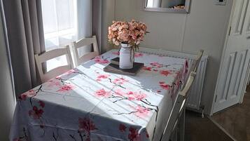 A dining area with a table set for two, a vase of flowers, and a mirror on the wall.