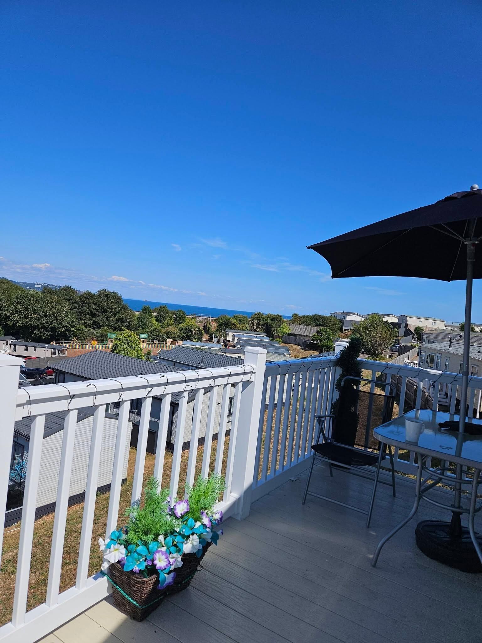 A deck with a white railing, a table with chairs, and a potted plant with flowers.