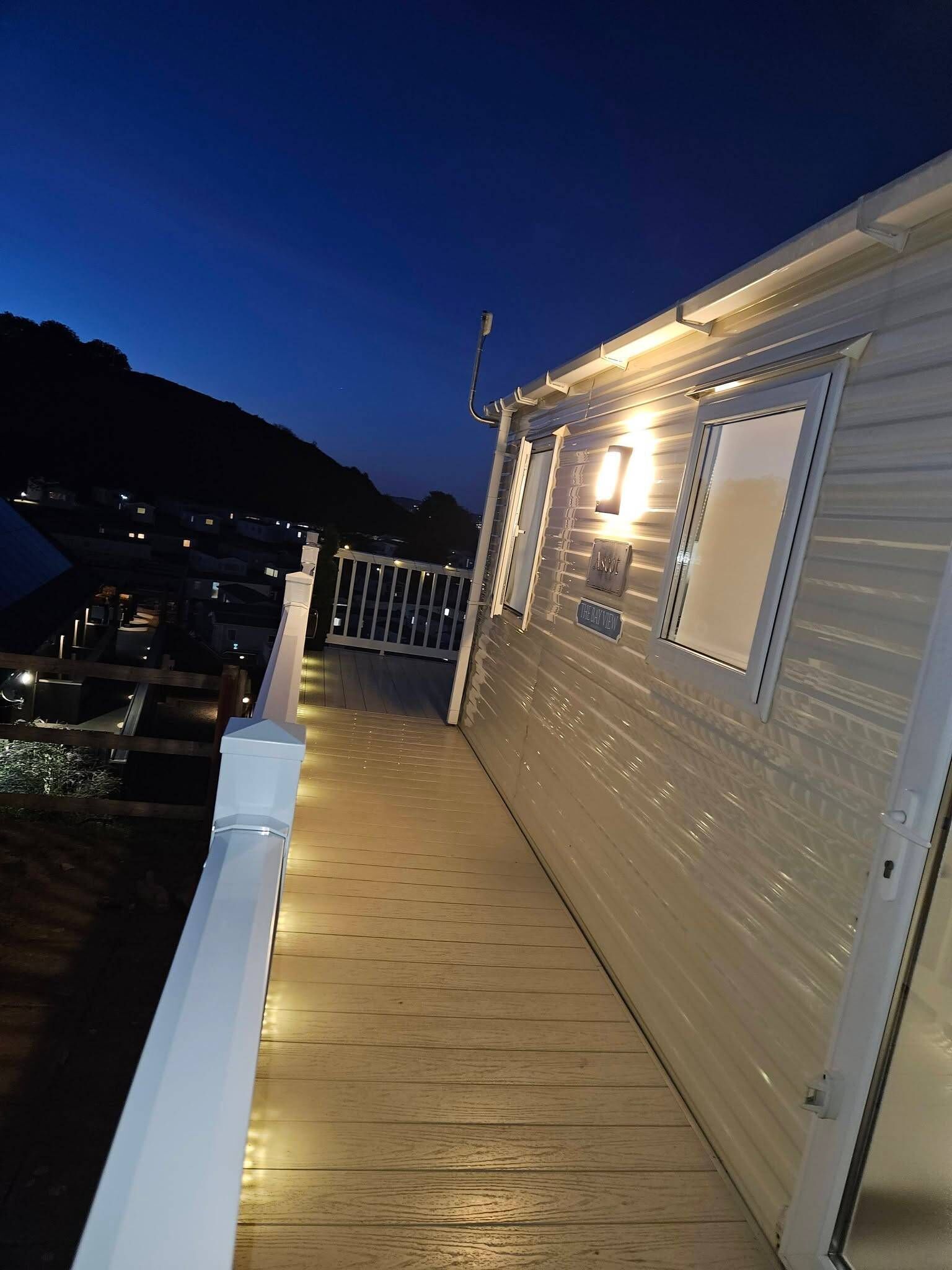 A wooden deck with a railing, a door, and a window on a building.