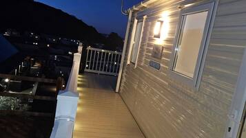 A wooden deck with a railing, a door, and a window on a building.