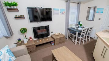 A living room with a flat-screen TV, a fireplace, a dining area with a table and chairs, and a kitchen area with a countertop.