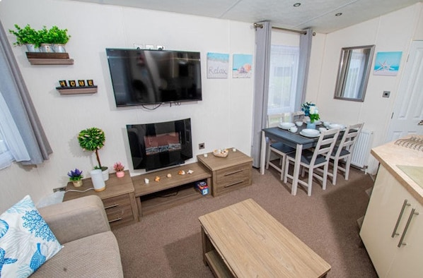 Una sala de estar con televisor de pantalla plana, chimenea, comedor con mesa y sillas, y área de cocina con mostrador.