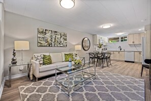A modern living room with a sofa, coffee table, and a dining area with chairs and a table. - Beautifully Remodeled 2 Bedroom Basement Apartment (Toronto)