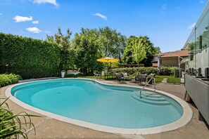 A swimming pool with a curved edge, surrounded by a patio area with outdoor furniture and a yellow umbrella. - Beautifully Remodeled 2 Bedroom Basement Apartment (Toronto)