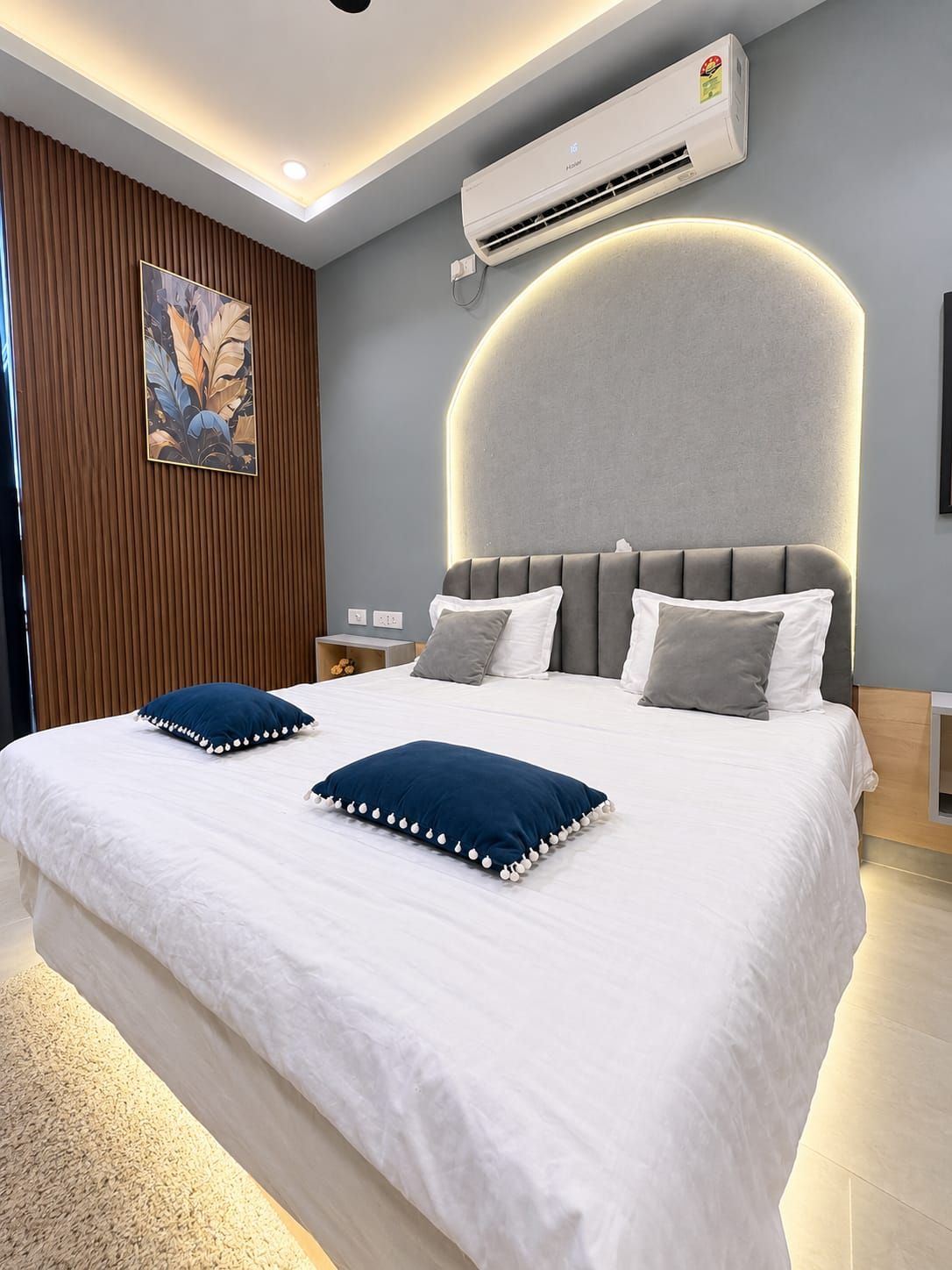 Un dormitorio moderno con una cama grande, un cabecero con iluminación integrada, un equipo de aire acondicionado y un panel decorativo en la pared.