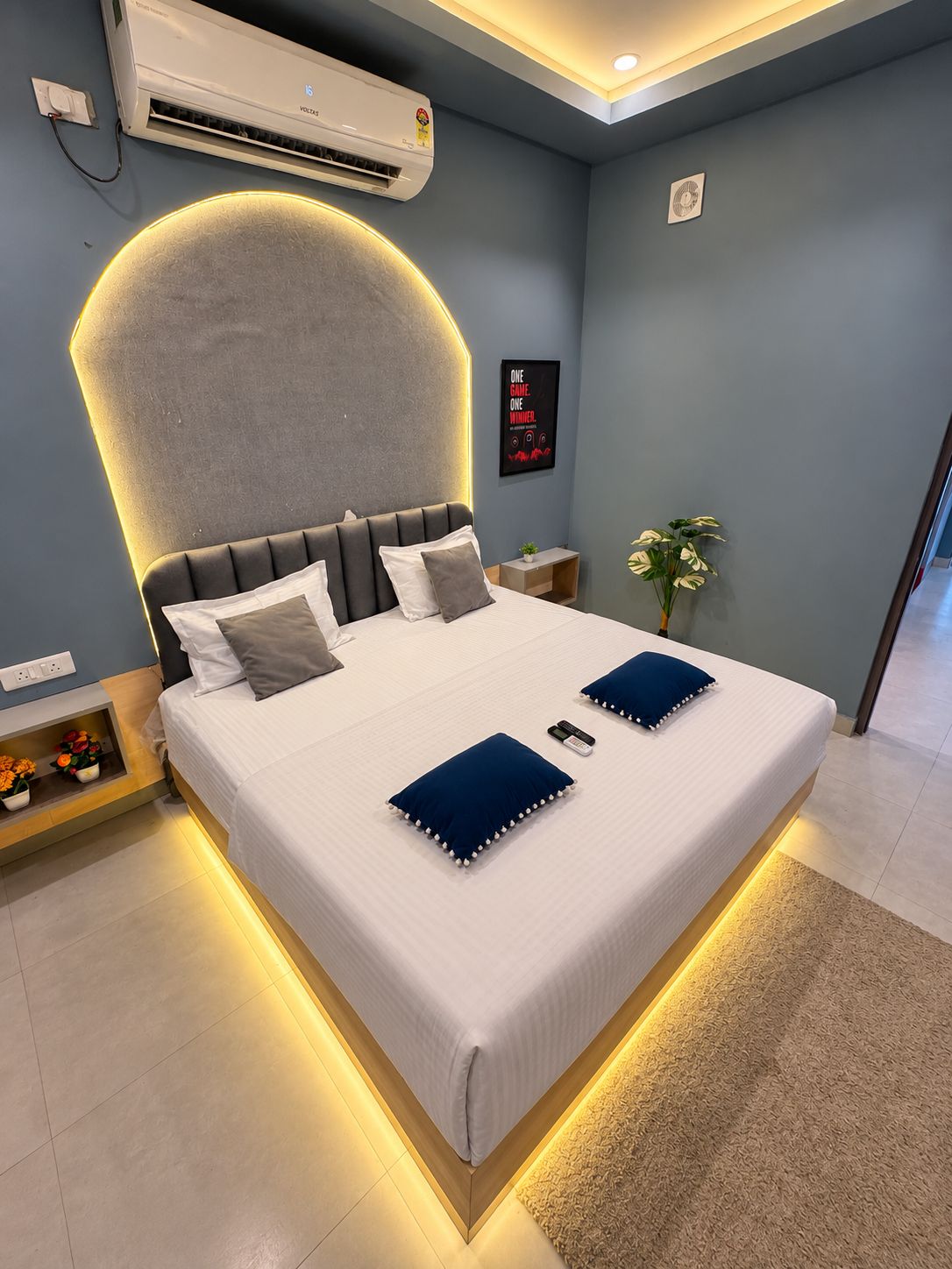 A modern bedroom with a bed, bedside tables, an air conditioning unit, a wall-mounted fan, and a poster.
